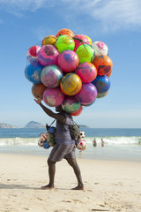 Beach vendor selling colorful beach balls carries his merchandise along Ipanema Beach