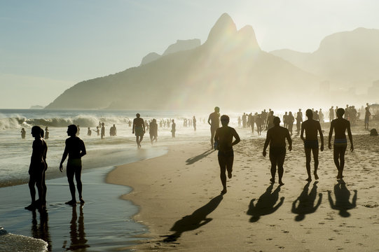 Silhouettes Of People Walking Along Golden Sunset Shores Of Ipanema Beach Rio De Janeiro Brazil