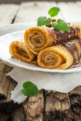 Pancakes with chocolate, nuts and mint leaf on an old wooden tab