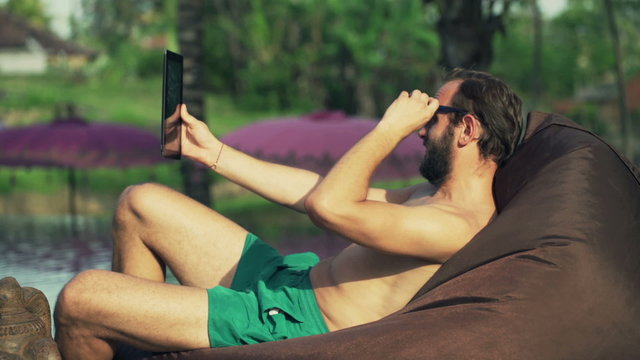 Young happy man taking selfie photo with tablet by the pool
