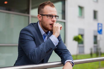 Portrait of young businessman with beard standing in front of office building.
