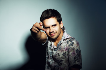 Fototapeta premium Studio portrait of a handsome young man in shirt posing in the spotlight over a grey background and showing middle finger 