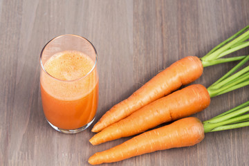 A glass of healthy carrot smoothie with carrots on wooden background