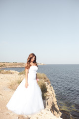 Fototapeta na wymiar Young beautiful bride posing outdoors. Standing at sea shore. Summer time. Wedding day. 