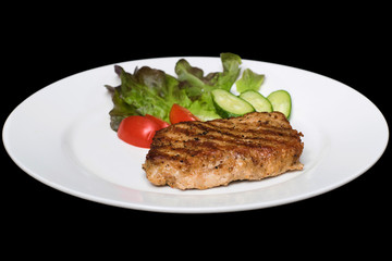 Photo of a pork stake on a white plate with a cucumber, tomato a