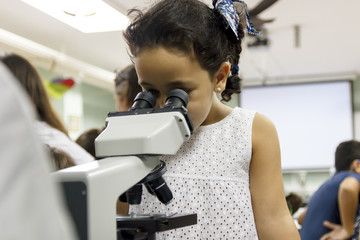 Experimentando en clase de biología. Niños investigando. Niña mirando por el microscopio....