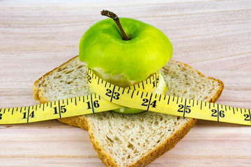 Apple on top of bread wrapped with measuring tape on wooden surface. Healthy diet concept. Selective focus.