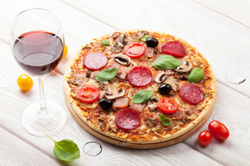 Italian pizza with pepperoni, tomatoes, olives, basil and red wi
