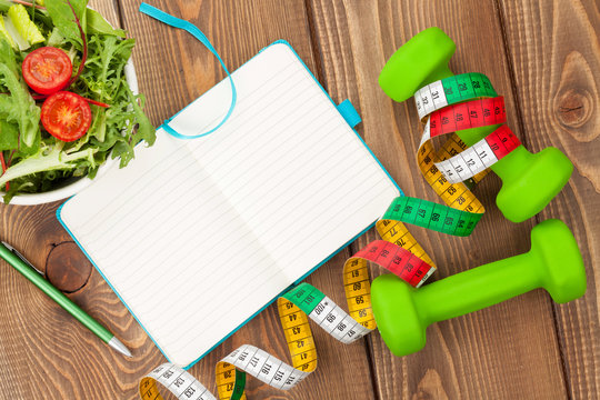Dumbells, tape measure, healthy food and notepad for copy space.