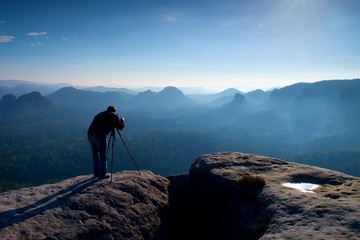 Professional on cliff. Nature photographer takes photos with mirror camera on peak of rock. Dreamy...