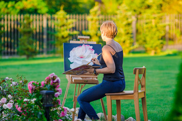 Happy woman painting a picture on an easel on a warm day