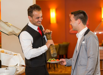 Catering service employee peppering meal at buffet in restaurant