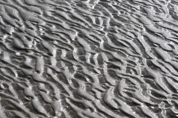 Pattern created by surf on dark beach sand.