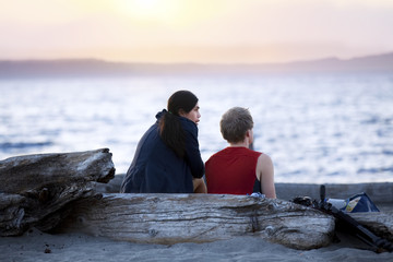Young couple  on driftwood log talking on beach at sunset