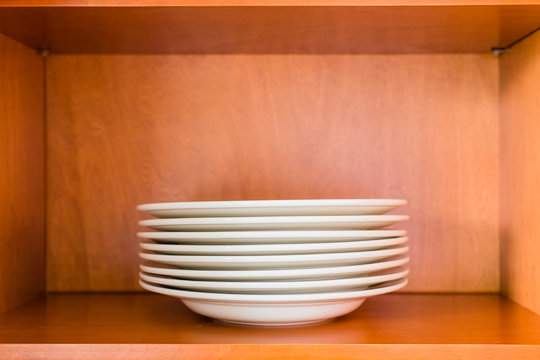 Organized Minimalistic Kitchen Cabinet With A Stack Of White Por