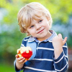 Funny blond kid boy eating healthy apple