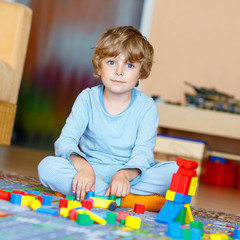 Little blond child playing with colorful wooden blocks indoor