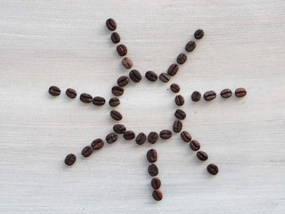 Coffee beans forming a sun with rays on grey wooden background
