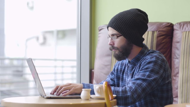 Young hipster fashion man working on laptop in coffee shop
