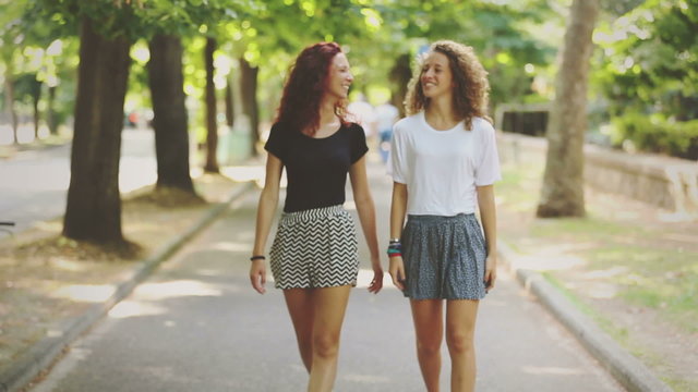 Two beautiful girls walking and laughing at park

