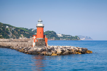 Fototapeta na wymiar Red lighthouse tower on the breakwater, Ischia