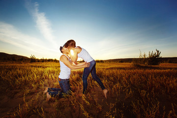 Young happy couple is kissing tenderly at golden summer sunset