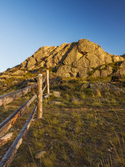 Fototapeta na wymiar Wooden fence and stone hill in the light of the setting sun