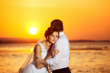 Beautiful bride is emracing elegant groom at sunrise