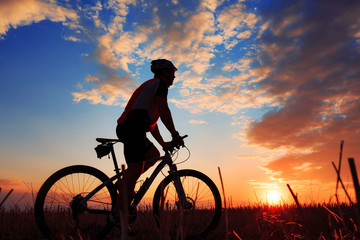 Obraz premium Silhouette of a biker and bicycle on sunset background.
