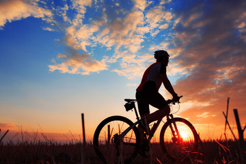 Obraz na płótnie Canvas Silhouette of a biker and bicycle on sunset background.