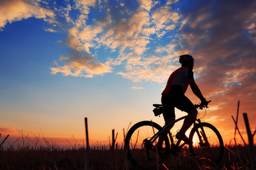 Fototapeta premium Silhouette of a biker and bicycle on sunset background.