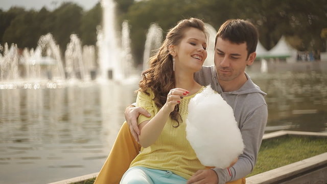lovers feed each other cotton candy in a park near the fountain