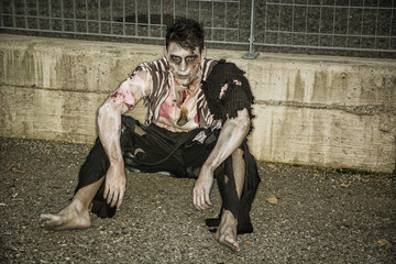 One male zombie sitting in empty city street on Halloween