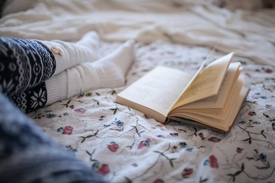 female legs in socks and book in bed