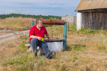Naklejka na ściany i meble Bearded senior man sitting at country draw-well in central Ukraine