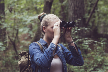 Young woman in forest observing with binocular.