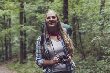 Plakat Happy blonde woman hiking in forest with vintage camera.