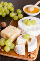 cheeses, honey, grapes and walnuts on a wooden background
