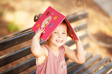 Portrait of laughing little girl with a book on his head