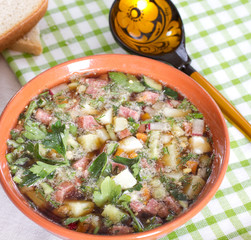 Okroshka on kvass in a ceramic bowl on a table and a wooden spoo