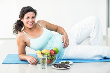 Portrait of pregnant woman lying by fruits and chocolates