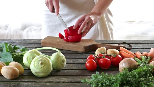 Woman slice vegetables. Woman slice paprika on wooden table. Rustic style.
