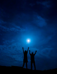 Fototapeta premium Silhouette of couple against full moon with hands up