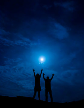 Silhouette of couple against full moon with hands up