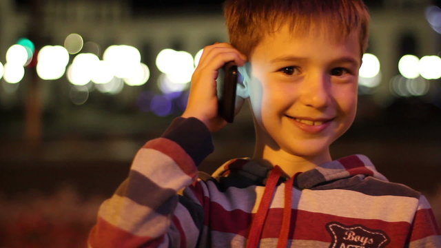 Small handsome boy 8 years old, talking on mobile phone at night