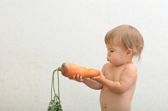 Little girl looking at carrot with doubt