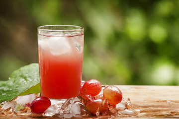Cold red grape juice on natural green background, selective focu