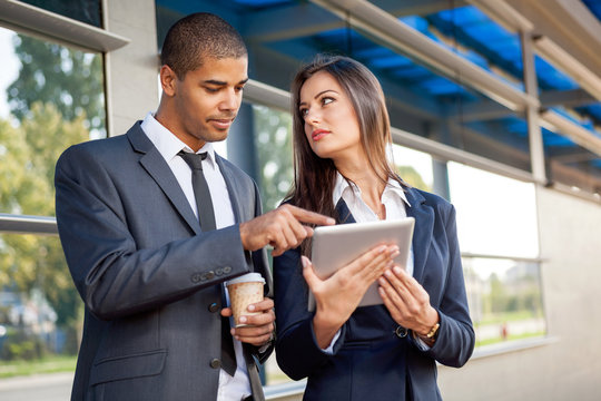 Business man and woman working outdoors with tablet computer in