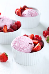 Ice cream in bowl with strawberries and raspberries on white woo