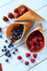 Waffle cones with berries on wooden table